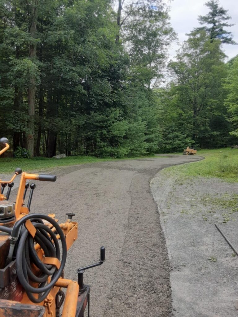 A freshly paved pathway through a forest area with construction equipment visible on the left and in the distance.